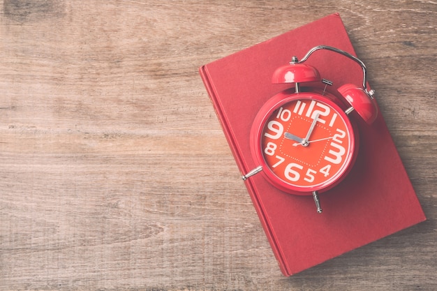 Top view book and red clock on wooden plank background. Time for reading concept