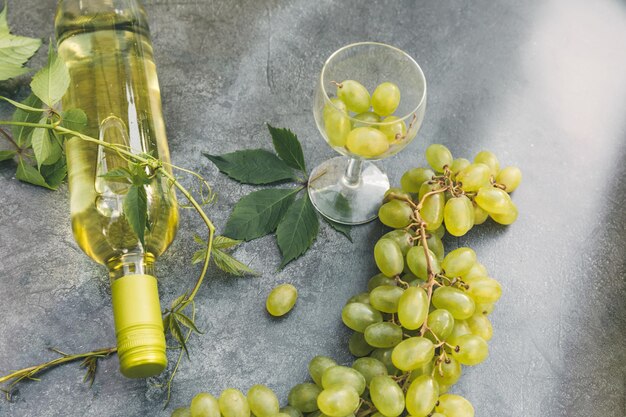 Top view of bottle white wine green vine wineglass and ripe grape on vintage gray stone table backgr...