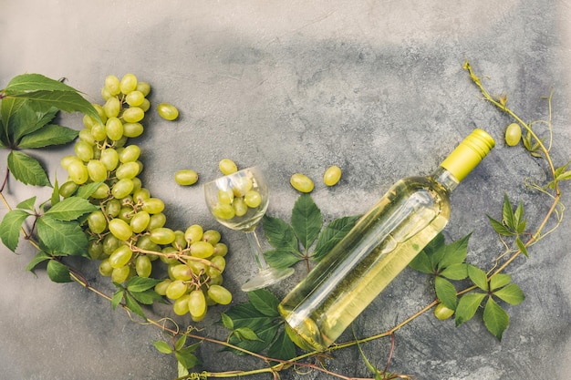 Top view of bottle white wine green vine wineglass and ripe grape on vintage gray stone table backgr...