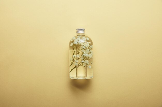 Вид сверху на бутылку с органическим косметическим продуктом и сушеными белыми полевыми цветами внутри на желтом