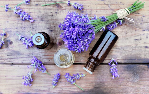 Top view on bottles of essential oil and bouquet of  lavender flower arranged on a wooden table