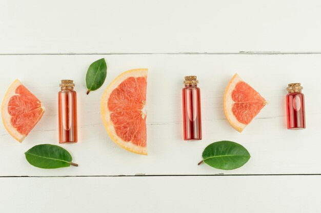 グレープフルーツのエッセンシャルオイルまたは化粧品のエッセンスとフルーツと緑の葉のスレートが入った蓋付きのボトルの上面図。フラットレイ。白色の背景。