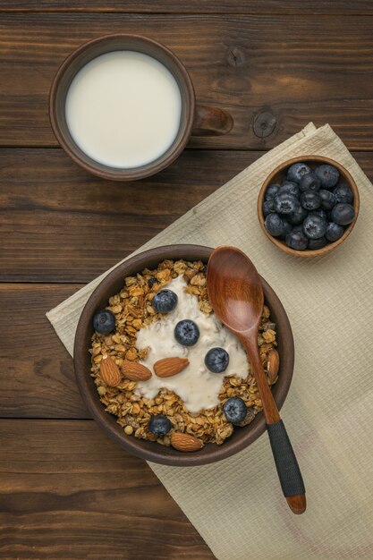 Top view of a bowl of muesli, a glass of milk and a bowl of blueberries on a wooden table. Flat lay.