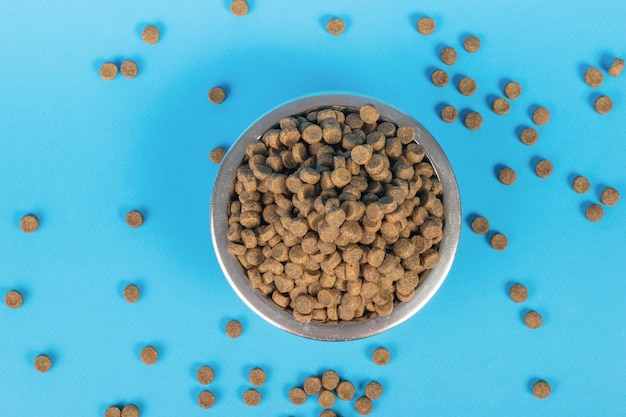 Top view of a bowl overflowing with dog food on a blue background