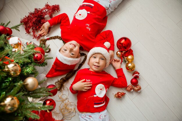 top view a boy and a girl in red pajamas are lying on the floor under the Christmas tree