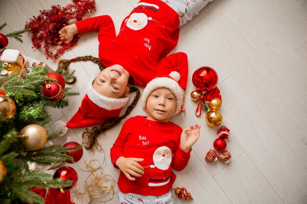 top view a boy and a girl in red pajamas are lying on the floor under the Christmas tree