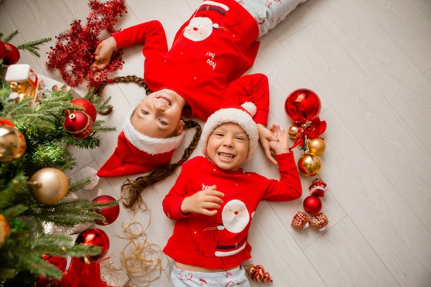 top view a boy and a girl in red pajamas are lying on the floor under the Christmas tree