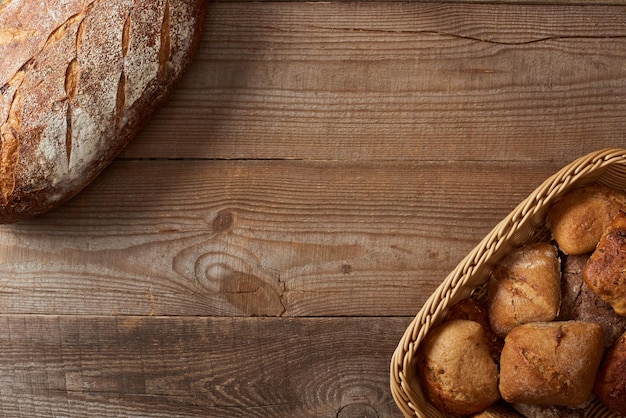 Top view of bread loaf and buns in wicker basket on wooden table