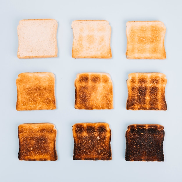 Top view of bread slices at varying stages of toasting on white background