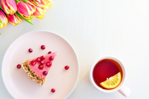 Top view for breakfast, morning with flowers tulips, cake, tea in pink mug on white background.