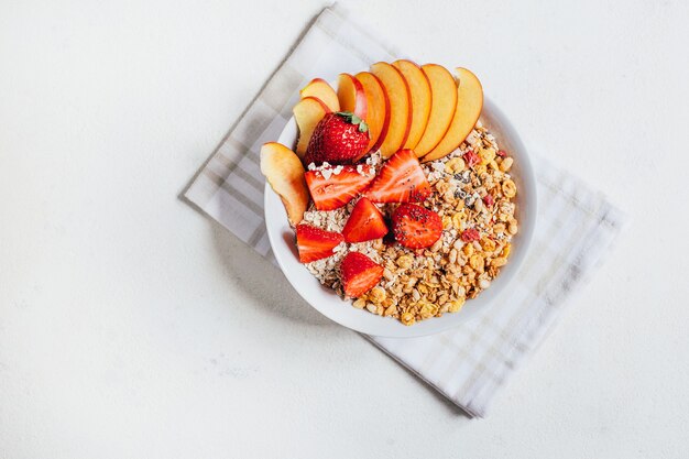 Vista dall'alto della farina d'avena di porridge per la colazione con fiocchi di muesli frutti fragole e pesche in un piatto bianco su sfondo bianco