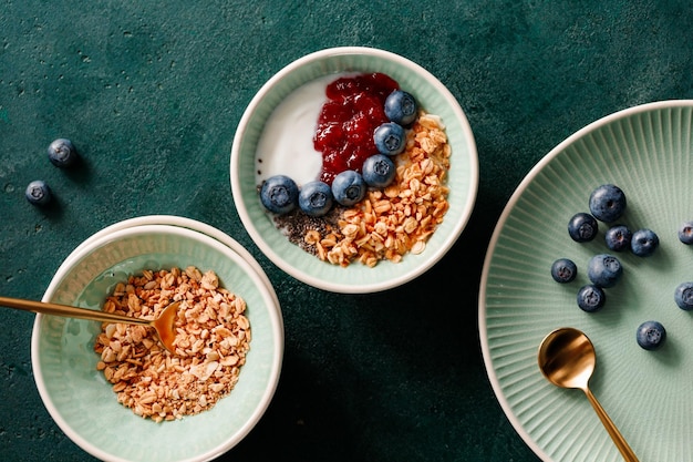 짙은 녹색 테이블에 그래놀라 요구르트 딸기 잼 치아 씨앗과 블루베리가 포함된 아침 식사의 최고 전망