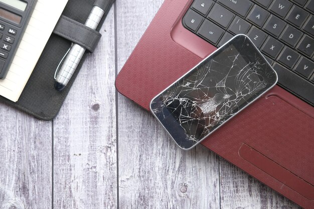 Top view of broken smart phone on laptop on table