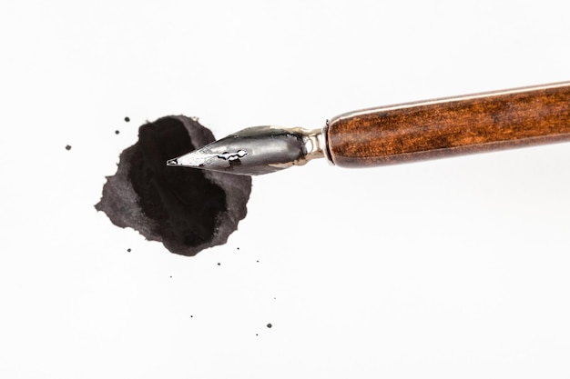 Top view of brown nib pen over black ink blot