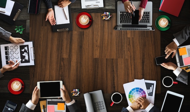 Top view of business Group of Multiethnic Busy People meeting with other in modern office with laptop computer, smartphone, tablet, coffee and document on table.