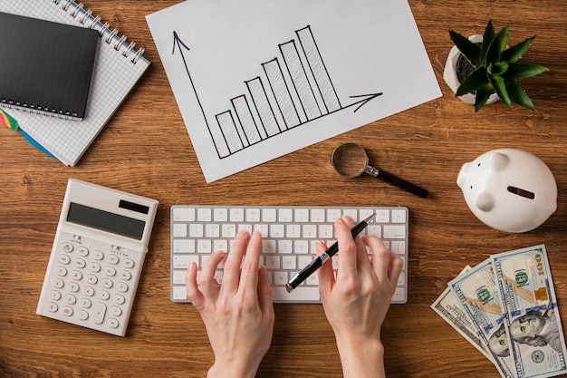 Top view of business items with growth chart and hands using keyboard