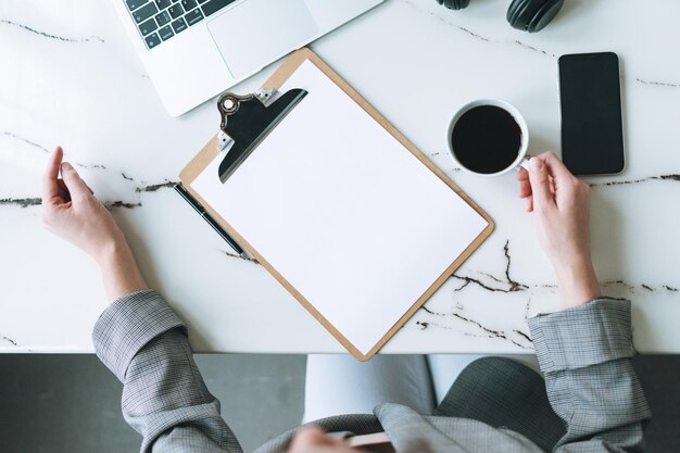 Top view of business woman on working place with cup of coffee notes open laptop smartphone on white marble table in the bright modern office room mockup