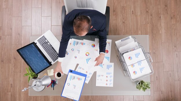 Top view of businessman holding cup of coffee while typing company statistics