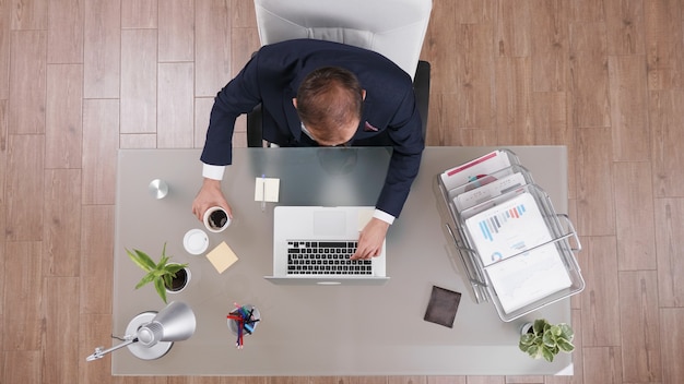 Top view of businessman holding cup of coffee while typing company statistics