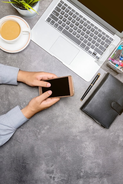 Top view of businessman using mobile phone with laptop, coffee, potted plant, notebook and business accessories