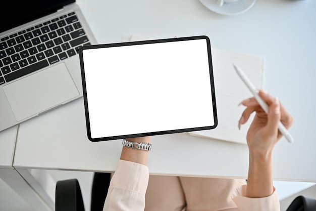 Top view of a businesswoman holding a digital tablet mockup and stylus pen over office desk