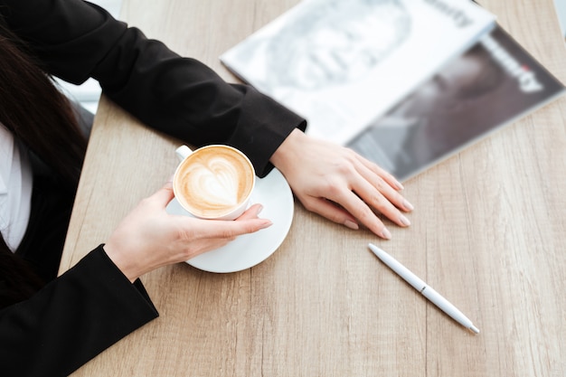 Top view of businesswoman sitting at table and drinking coffee