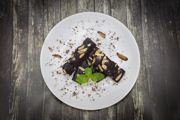 Vista superiore dei brownie del cioccolato del dolce con i dadi e della menta sul piatto bianco e sul backgroun di legno