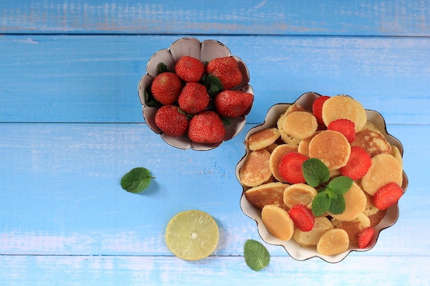 Alzata per torta vista dall'alto con piccoli cereali per pancake e fragole, guarnita con foglie di menta su sfondo bianco. cibo alla moda. mini pancake ai cereali. orientamento orizzontale