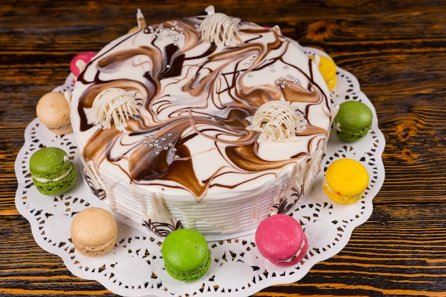 Top view of cake with different white chocolate ornaments, near macarons, on wooden desk