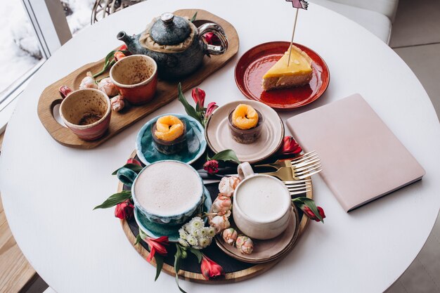 Top view of cakes and cups of coffee with notebook in cafe