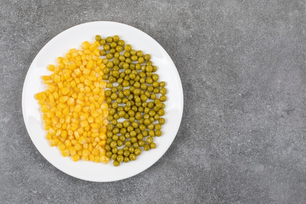 Top view of canned corn seed and green pea on white plate