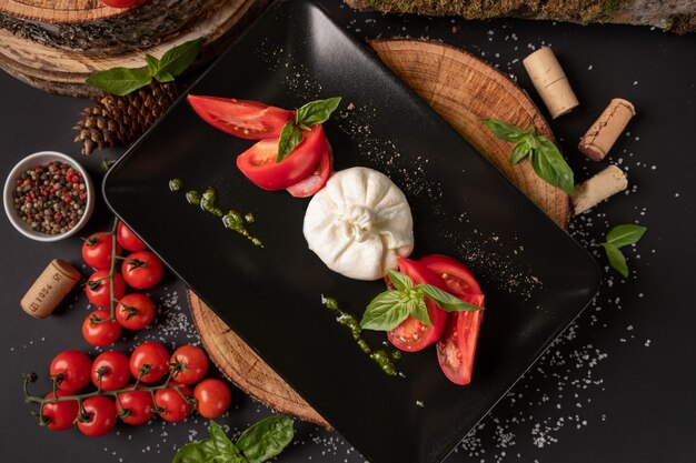 Foto vista dall'alto insalata caprese. mozzarella, pomodori e basilico foglie di erbe sulla banda nera su legno