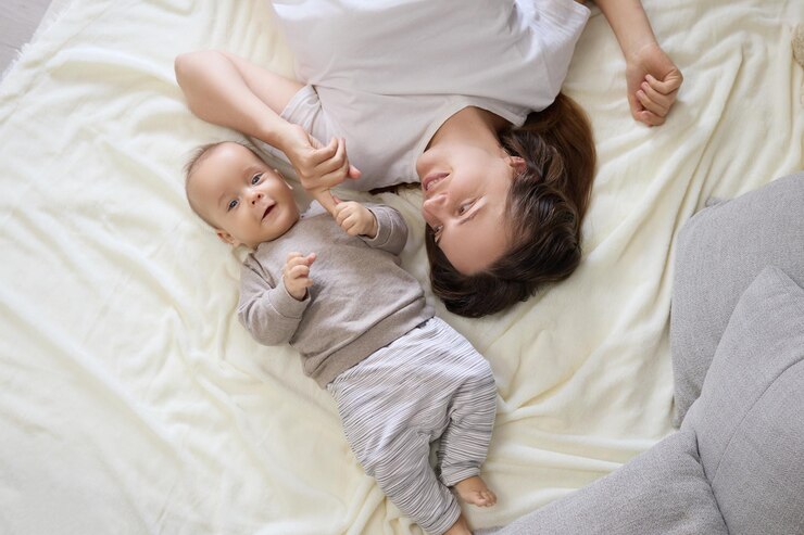 Photo 백인 어머니가 어린 아기 딸이나 아들과 함께 침실에 누워서 행복과 순수함으로 가득 찬 놀이로운 환경을 만들고 가족을 결합시니다.