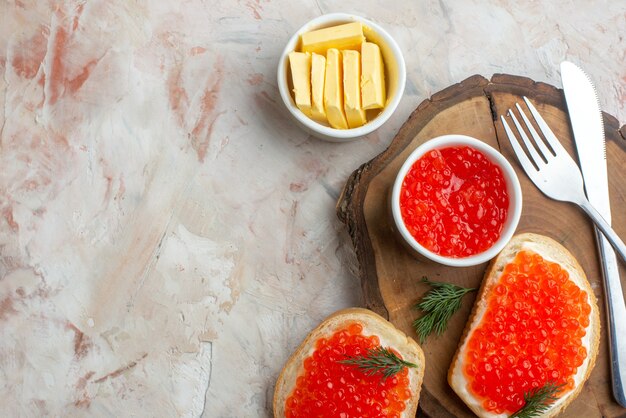 бутерброды с икрой, столовыми приборами и сыром на разделочной доске на светлой поверхности