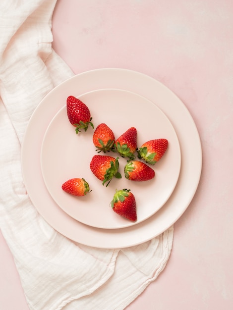 Top view of ceramic plates with strawberries on pink pastel background