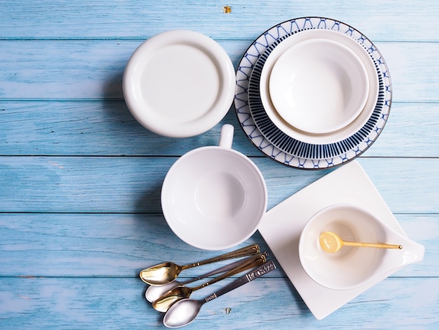 Top view of ceramic tableware set with round dish plates, crockery tea cup bowl and teaspoons on wooden table.