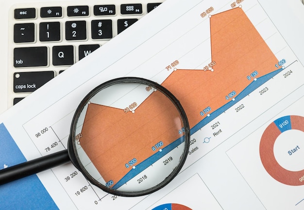 拡大鏡とラップトップを使用したチャートの上面図スプレッドシート財務開発グラフ銀行口座統計経済学データ分析投資分析証券取引所
