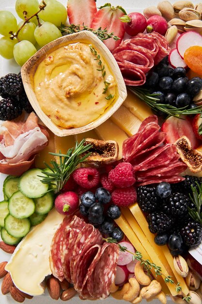 Foto vista superiore di una tavola di formaggio con frutta e verdura hummus su uno sfondo bianco