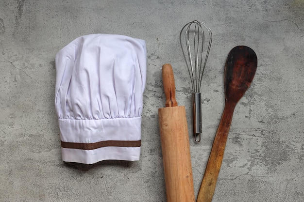 Vista dall'alto del cappello da chef e utensili da cucina su sfondo grigio rustico