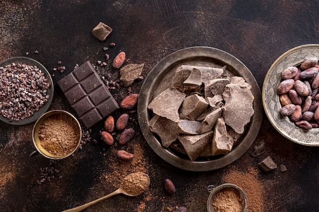 Photo top view of chocolate chunks on plate with cocoa beans and powder