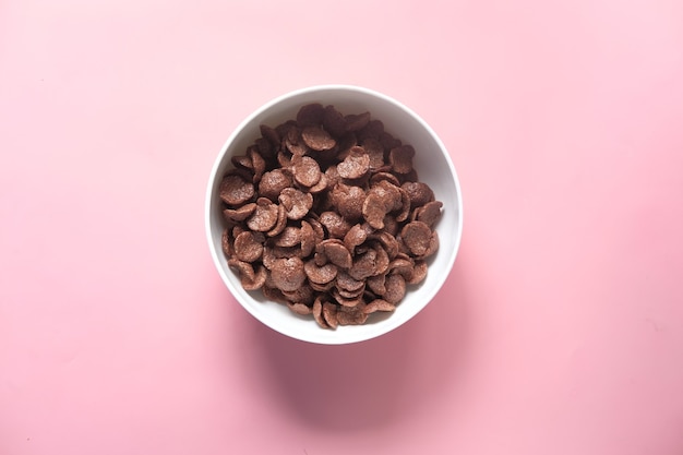 Photo top view of chocolate corn flakes in a bowl on pink .