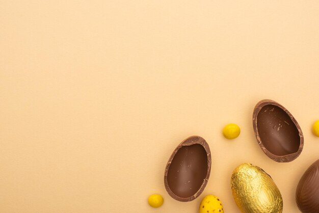 Top view of chocolate and quail eggs with yellow sweets on beige background
