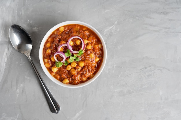 Top view of chole masala vegan food of chickpeas and tomatoes in bowl with spoon on concrete table