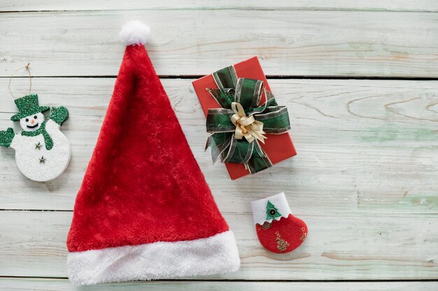 Top view of Christmas composition with red santa claus hat, snow doll, gift boxes on wooden background and copy space. Accessories of Christmas and new year concept.