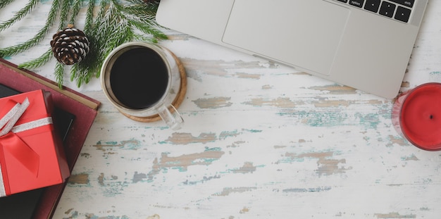 Photo top view of christmas decorated workplace  with laptop computer, coffee cup and present on vintage wooden desk