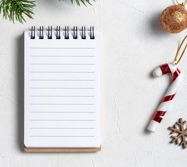 Vista dall'alto dello sfondo delle decorazioni natalizie con un taccuino bianco sullo sfondo della tavola bianca con spazio per le copie, concetto di celebrazione delle vacanze.