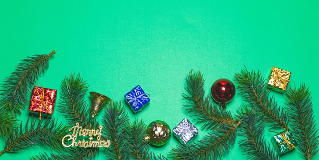 Top view of Christmas gift box red balls with spruce branches and bell on green background