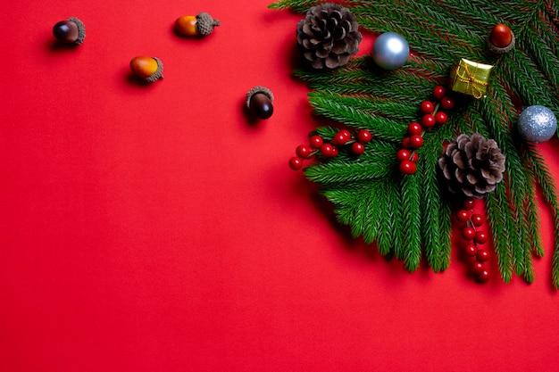 Top view of Christmas gift boxes with pine cones, red berries and fir tree on red paper background.