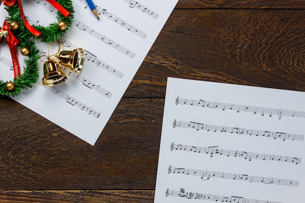 Top view christmas music note paper with christmas wreath on\
wooden background and copy space.