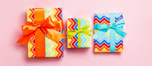 Top view christmas present box with blue green and orange bow on pink background